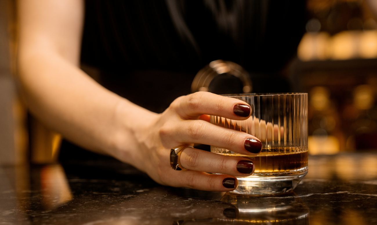 A glass of Scotch whisky held elegantly by a woman's hand, symbolizing sophistication and the enjoyment of premium whisky.